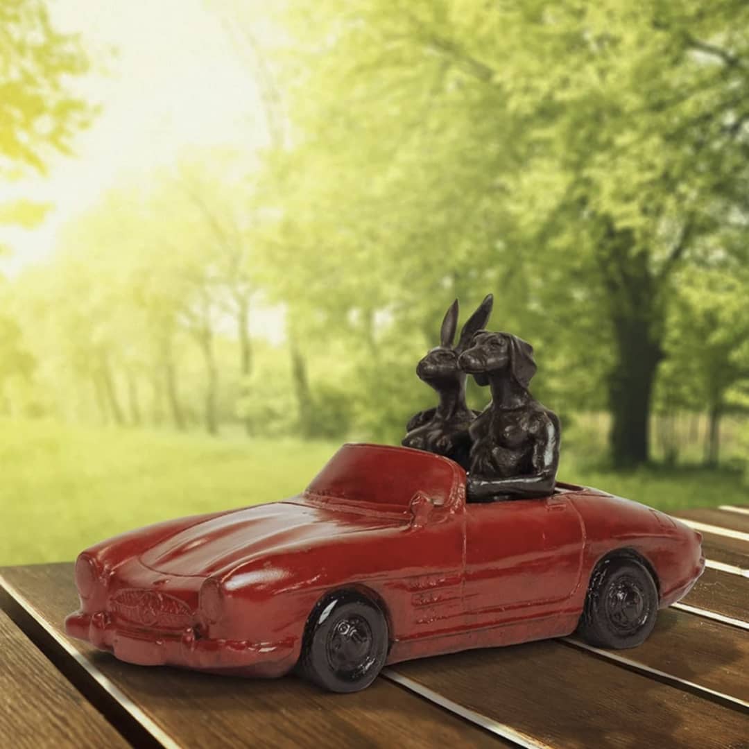 Gillie and Marc Bronze Sculpture ~ 'They Loved Breaking the Speed Limit' - Curate Art & Design in Daylesford, Gillie and Marc's premier gallery in Victoria.

A small red convertible car figurine with two black dog statues seated inside, placed on a wooden surface with a blurred green outdoor background.