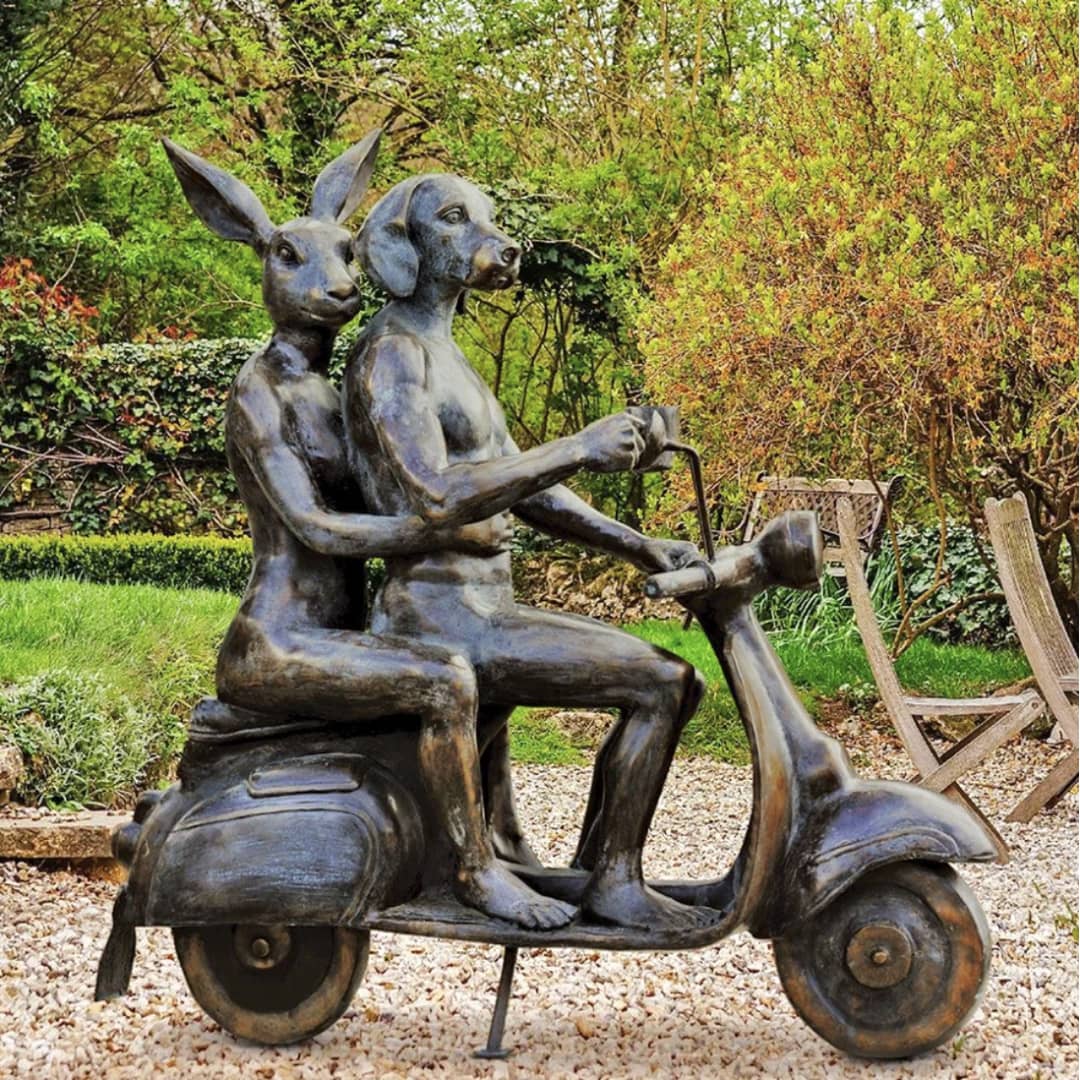 Gillie and Marc Public Art Sculpture ~ 'It Takes Two'.
Bronze sculpture of two people on a scooter in a garden setting